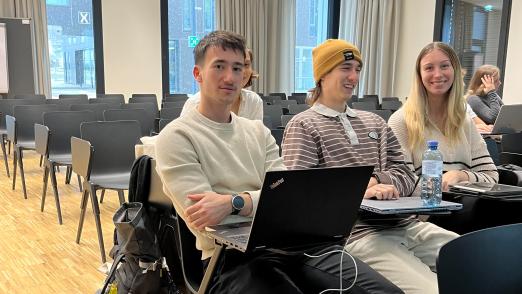 Uniluft schnuppern - Drei Schüler:innen sitzen im Vorlesungssaal und lächeln in die Kamera