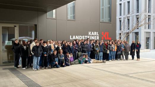 Schulbesuch Piaristengymnasium - Schüler:innen stehen vor dem KL Gebäude, im Hintergrund das KL Logo
